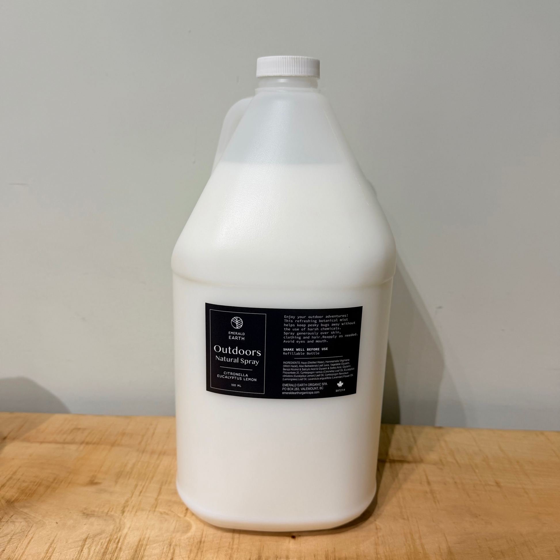 A large white plastic jug of Outdoor Natural Bug Spray standing on a light wood surface against a plain light gray wall.