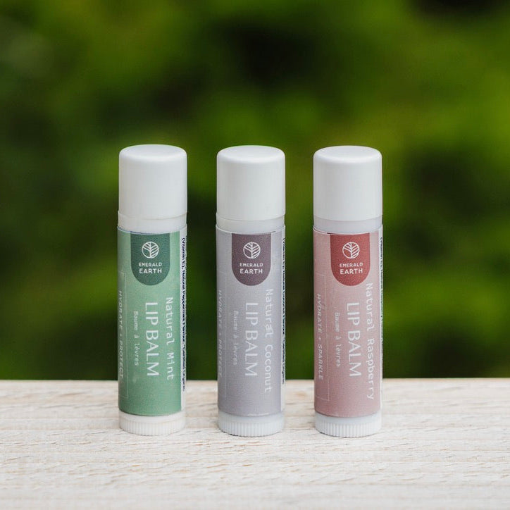 Three lip balm tubes on a wooden surface with a blurred green background