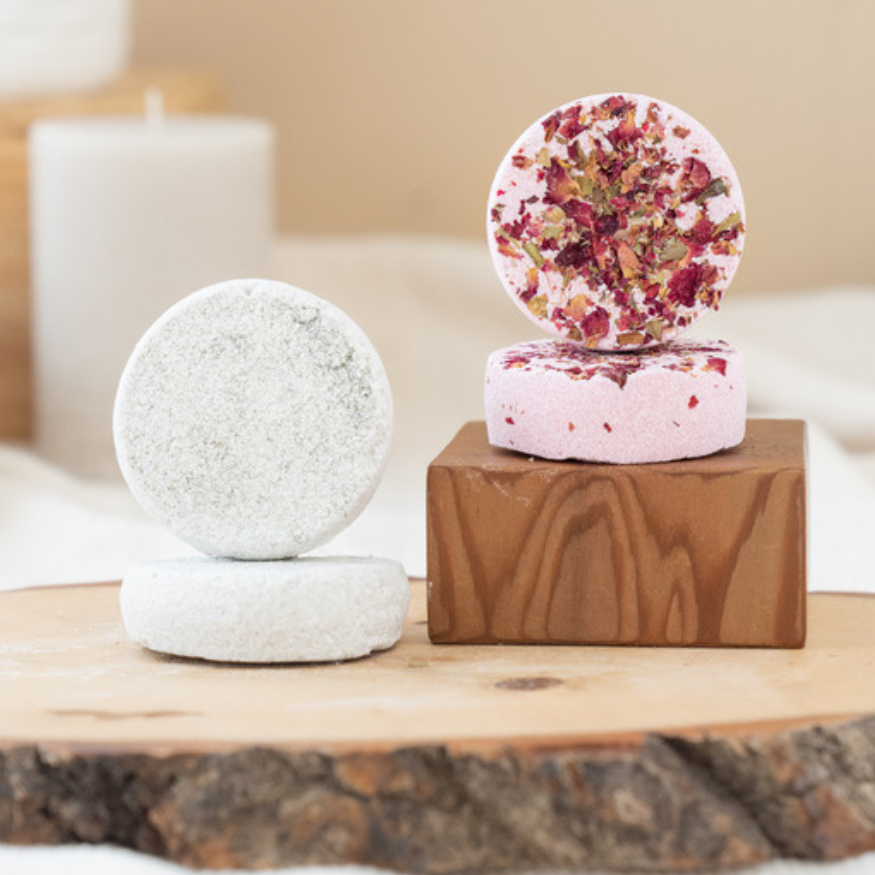 A bath truffle with rose petals on top, presented on a wooden block, with another truffle and a candle in the background.