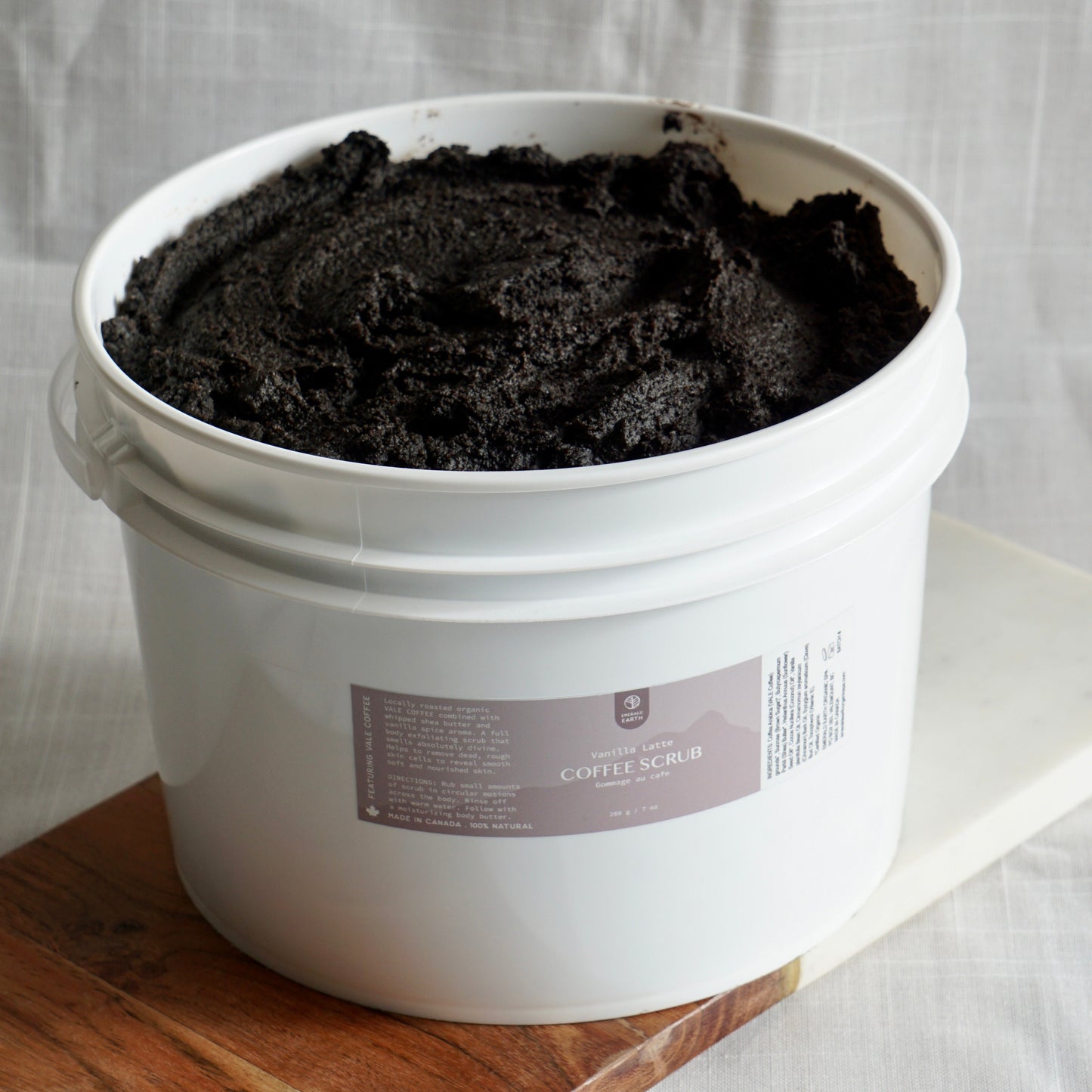 White bucket filled with dark material on a wooden surface with a white curtain background