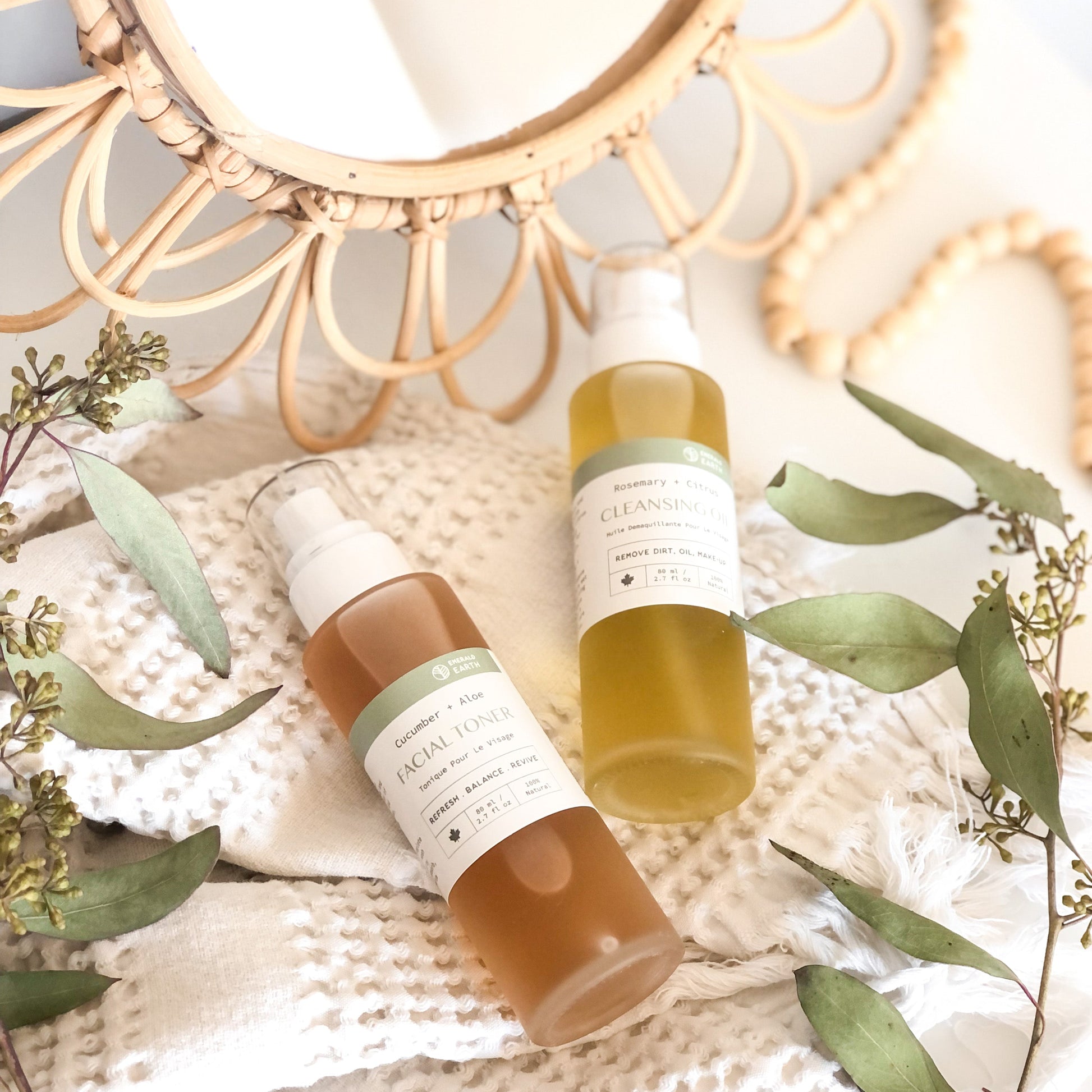 Two skincare bottles on a textured surface with green leaves and a decorative mirror in the background.
