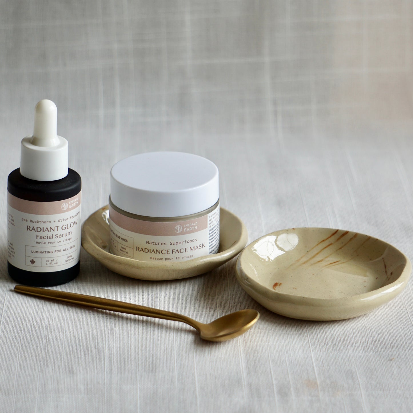 Cosmetic products including a dropper bottle, jar, and face mask on a textured surface.