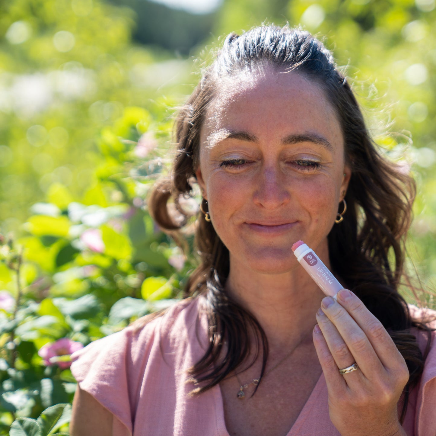 Woman holding natural lip balm in a garden setting