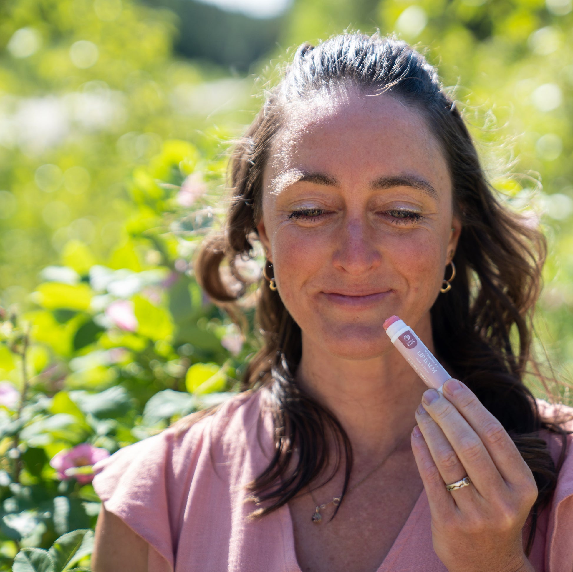 Woman holding natural lip balm in a garden setting