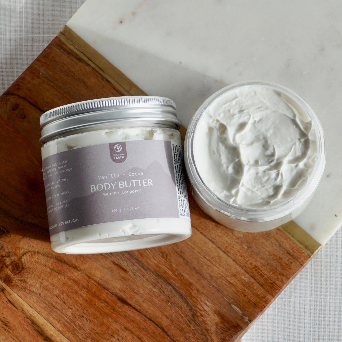 Two containers of body butter on a wooden board with a marble edge.