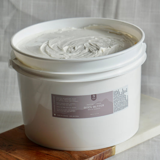 White bucket of body butter on a wooden surface with a neutral background
