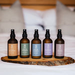 Five bottles of diffuser on a wooden tray with a blurred bed background