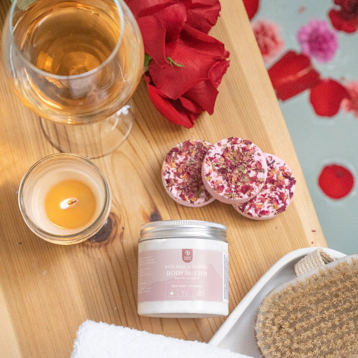 Wooden tray with a glass of white wine, candles, bath bombs, body butter and a towel on a decorative background with flowers.