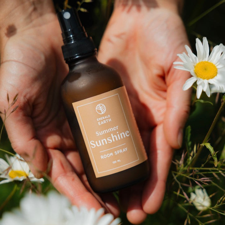 Bottle of 'Summer Sunshine' spray held between hands with daisies in the background