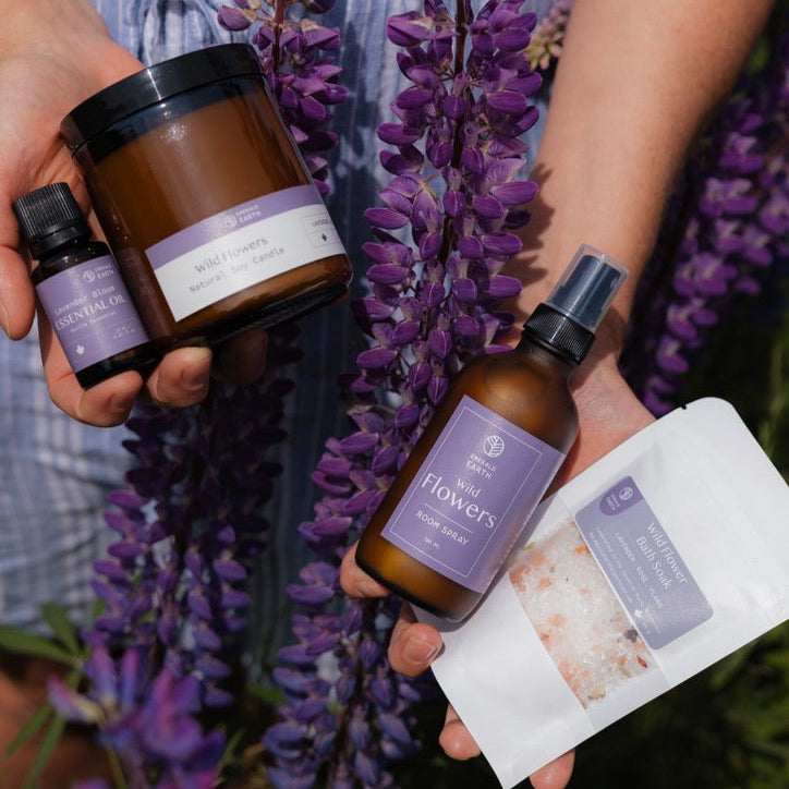 Person holding various skincare products with a background of purple flowers