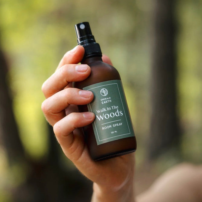 Hand holding a bottle labeled 'Walk in the Woods' against a blurred forest background